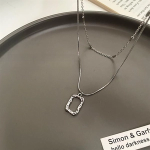 Detail of double-layer silver necklace with hammered rectangle pendant on grey tray