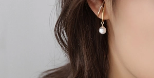 Nahaufnahme goldener Ohrklemmen mit Kunstperlen-Anhänger und Strasssteinen für Damen
