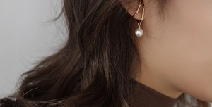Detail eines eleganten Gold-Ohrclips mit weißer Perle und Mikrodiamanten am Ohr