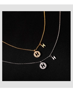 Gros plan de pendentifs ronds lettre H en or et argent sertis de diamants sur fond noir