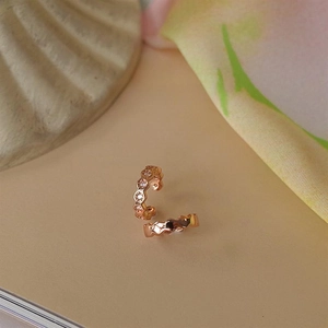 Macro shot of rose gold honeycomb ear cuff with small white zircons on beige background