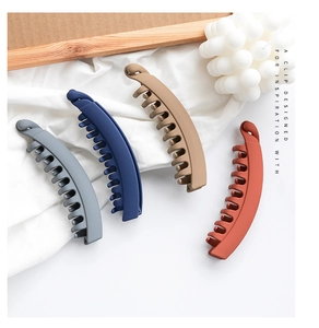 Detail view of four matte banana hair clips in dark Morandi colors on white fabric