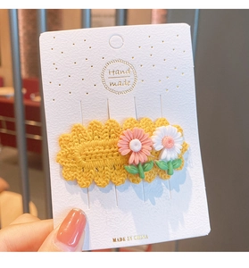 Detailed macro view of a yellow knitted floral hair clip featuring pink and white daisy decors
