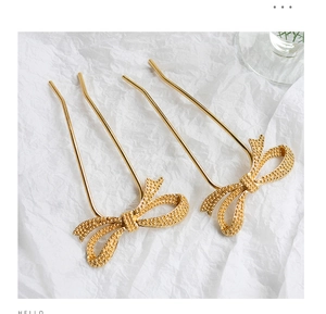 Detail of golden U-shaped hairpins with textured bow design on a white background