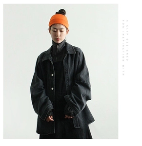 Close-up of vibrant orange knitted beanie paired with a black denim jacket and silver buttons