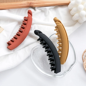 Matte banana hair clips in brick red, black, and yellow on a minimalist background