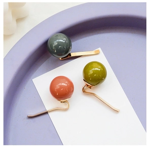 Detailed view of three minimalist gold hair clips with large pearl-like beads in various colors