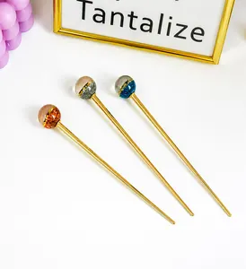Détail de trois épingles à cheveux en métal avec boules en résine pailletée et cadre doré