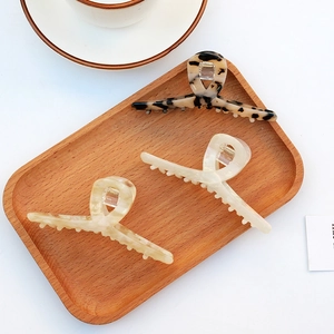Three large tortoiseshell and cream acetate hair claw clips arranged on a wooden tray