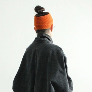 Minimalist orange knitted headband for women styled with a dark grey tweed jacket