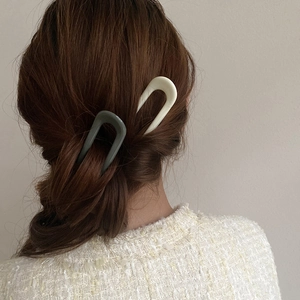 Modern U-shaped resin hair pins in cream and dark green colors on a low ponytail