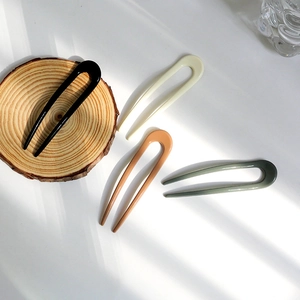 Minimalist U-shaped hair fork in four colors displayed on a wooden tray with shadows