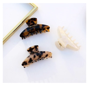 Three acetate triangle hair claws in tortoiseshell and cream finishes on white surface