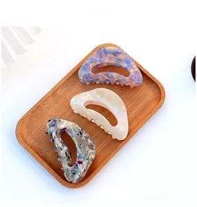 Three acetate hair claws in marble and pearl finishes on a wooden tray detail view