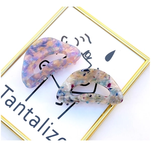Close-up of D-shaped acetate hair claws with artistic terrazzo patterns in pastel colors