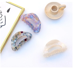 Detailed view of large acetate hair claws in lavender, grey-blue, and pearl white colors