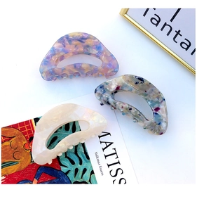 Three elegant acetate hair claws in diverse floral and marbled patterns on artistic background