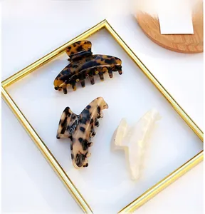 Three acetate hair claws in leopard and pearl patterns displayed in a gold tray