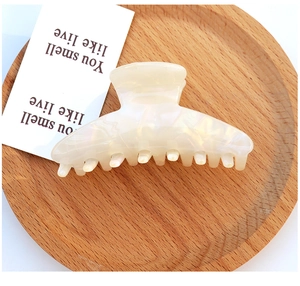 Macro detail of a cream-colored acetate hair claw clip with pearl luster finish on wood