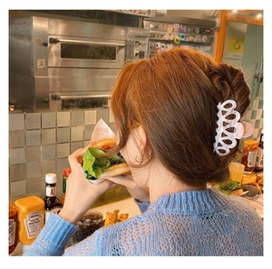 Detail of large white hollow-out acetate hair claw clip worn on a woman's thick hair