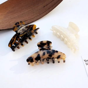 Three acetate hair claws in leopard, tortoiseshell, and cream white displayed on table