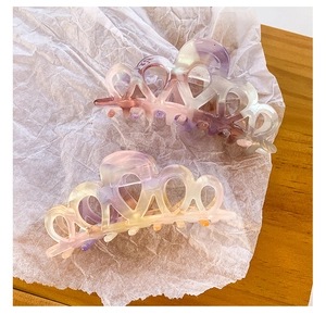 Detailed view of two marble patterned acetate hair claws on white paper and wood surface