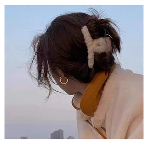 Detail of plush off-white hair claw clip and gold hoop earrings on a model