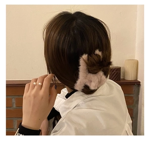 Detail of soft pink plush hair claw clip and gold double pearl ring on model in warm room