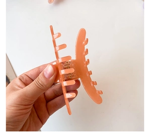 Detailed view of large orange-pink acetate hair claw clip held open by hand