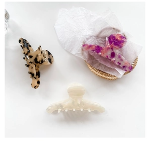 Three acetate hair claws in leopard, marble, and cream finishes on a woven tray