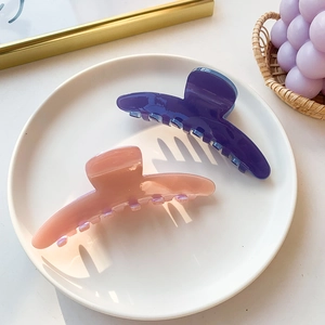 Glossy candy-colored acetate hair claws in purple and pink displayed on a white plate