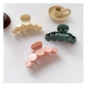 Close-up of three glossy hair claws in beige, green, and pink colors on a white desk
