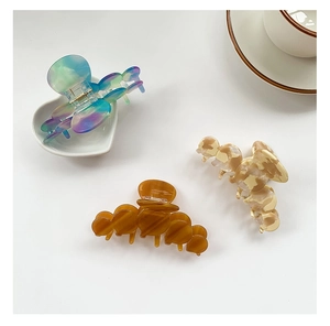 Three acetate hair claws in marble, amber, and gradient blue on a white vanity setup