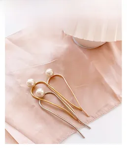 Détail de trois épingles à cheveux en métal en forme de U avec perles sur satin rose