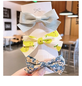 Détail de trois pinces à cheveux à nœuds en tissu avec motifs citrons et fleurs sur carte