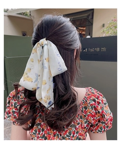 Détail d'un foulard en satin blanc imprimé fruits noué en nœud sur une queue de cheval