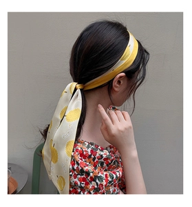 Gros plan d'un foulard en satin jaune à motif durian porté sur une queue de cheval