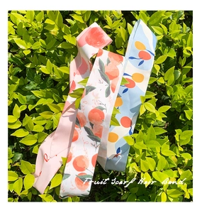 Détail de longs foulards en soie aux motifs de fruits et de pêches sur des feuilles vertes