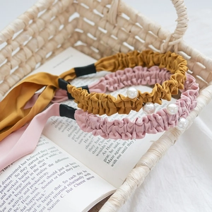 Détail de serre-têtes en tissu plissé avec perles blanches et longs rubans rose et jaune