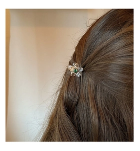 Dettaglio molletta a camelia con petali trasparenti e gemma verde su capelli castano scuro