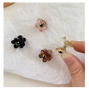 Dettaglio di quattro mini mollette per capelli a camelia in vari colori con gemma verde