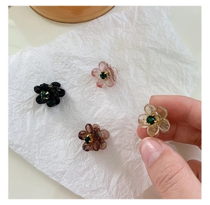 Primo piano di quattro mini fermagli per capelli a camelia con gemme in resina verde su carta