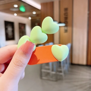 Détail d'une jolie barrette orange ornée de cœurs verts en résine au fini mat soigné