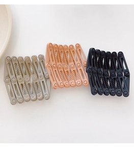 Detail of three matte foldable bird nest hair clips in grey, pink, and black colors