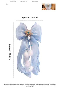 Détail de pince à nœud en organza bleu clair avec cœur en gemme verte et pompons blancs