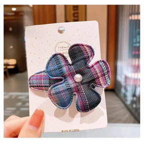 Gros plan d'une barrette fleur à carreaux bleus avec perle sur une carte blanche