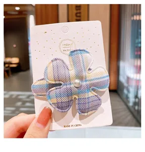 Détail d'une pince à cheveux fleur en tissu à carreaux avec perle centrale