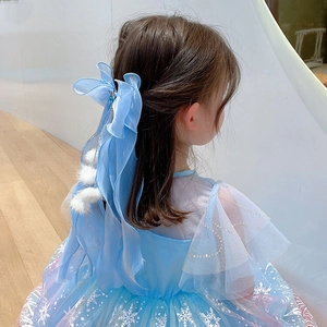 Nœud à cheveux en maille bleue avec pompons et glands porté par une jeune fille