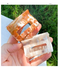 Close-up of two marbled acetate hair claws in orange and off-white with hollow design