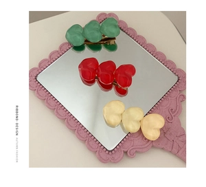 Detailed view of three resin heart hair clips in green, red and yellow on a mirror